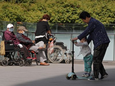 Женщина играет с ребенком рядом с пожилыми людьми в инвалидных колясках в Пекине. Фото: Andy Wong / AP