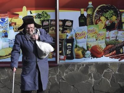 Пожилой мужчина идет с сумками из магазина. Витрина продуктового магазина. Фото: Виктор Коротаев / Коммерсант